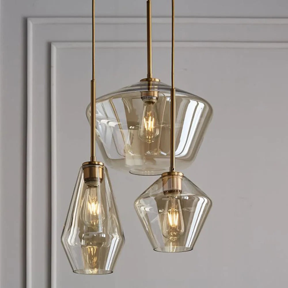 Three Clérachic faceted glass pendant lights in amber clustered at staggered drops against a panelled wall.