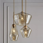 Three Clérachic faceted glass pendant lights in amber clustered at staggered drops against a panelled wall.
