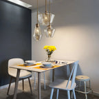 A trio of Clérachic faceted glass pendant lights over a set dining table, dark blue wall and yellow flowers below.