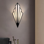 Clérachic black Art Deco wall lamp with fan-shaped linen panels lit warm on a taupe wall above a sofa arm and a plant stem.