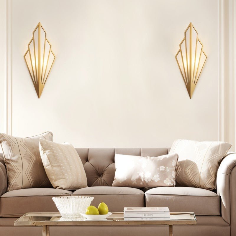 Pair of Clérachic gold Art Deco wall lamps flanking a cream wall above a buttoned taupe sofa and a glass coffee table.