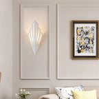 Clérachic white Art Deco wall lamp lit warm inside a panelled wall frame, with abstract art and cushions in the living room.