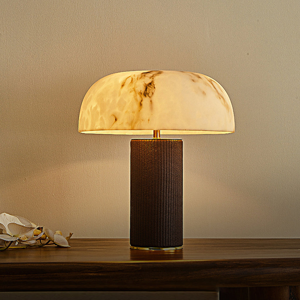 Lit domed shade with brown veining on a Clérachic table lamp, standing on a dark wood console against a warm wall.