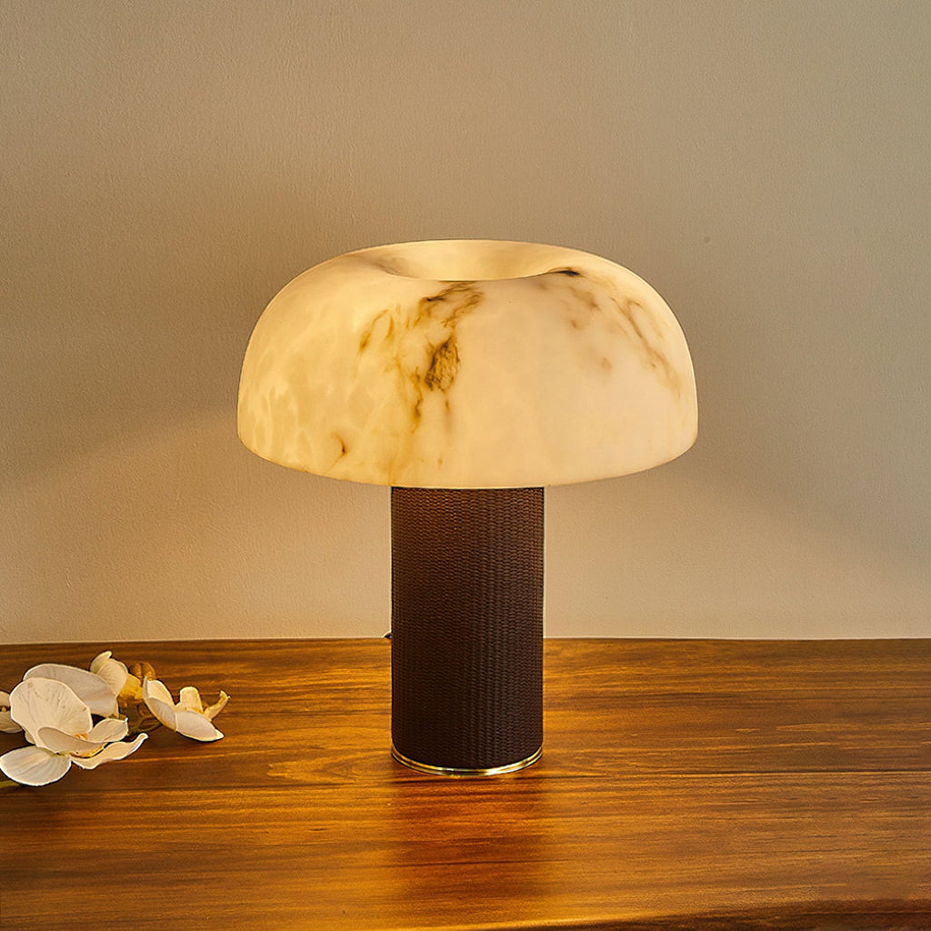 Slightly raised view of a Clérachic table lamp lit, with a softly glowing mushroom-shaped shade and a dark woven base.