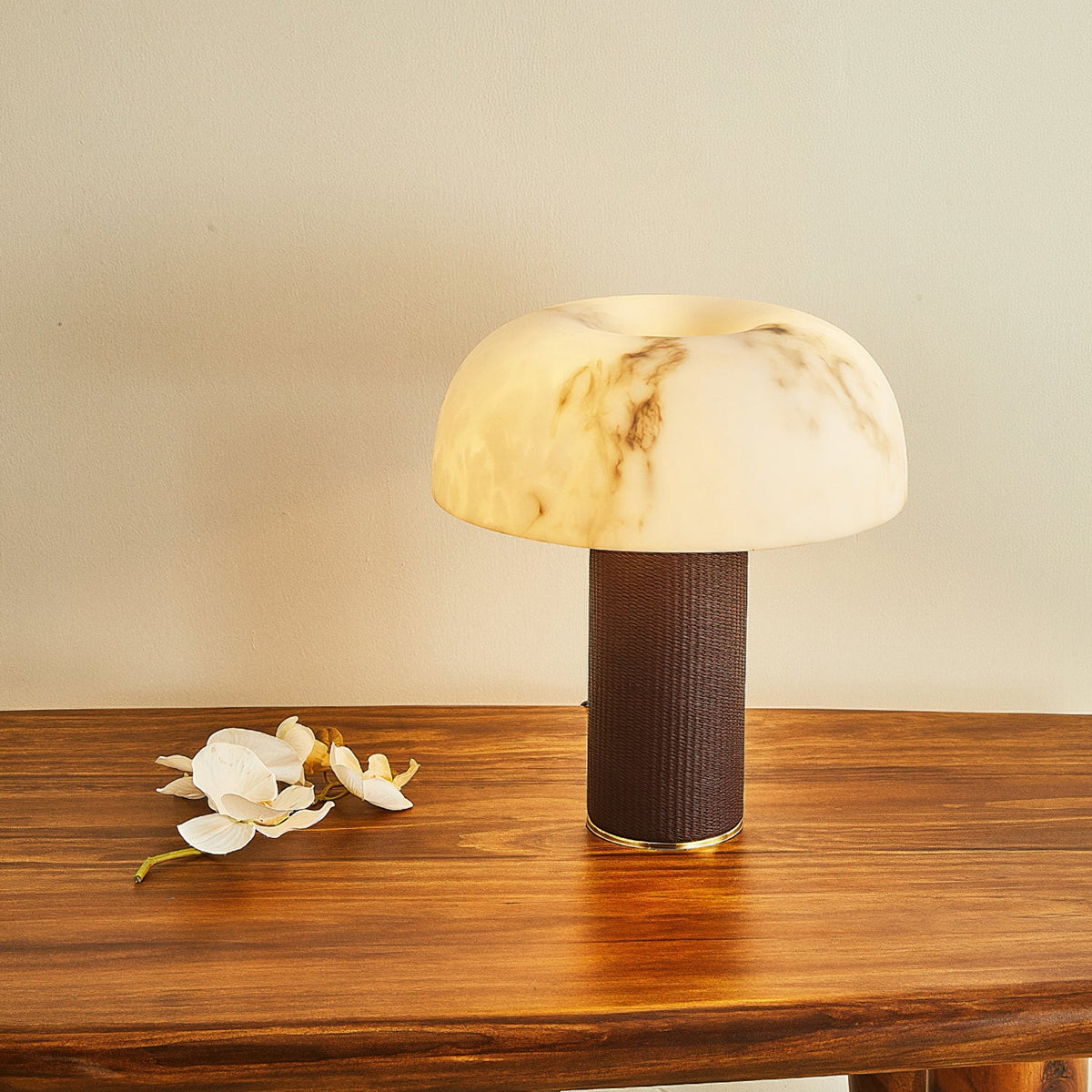 A Clérachic table lamp with a glowing domed shade sits low on a wooden table, with white orchid flowers beside the base.
