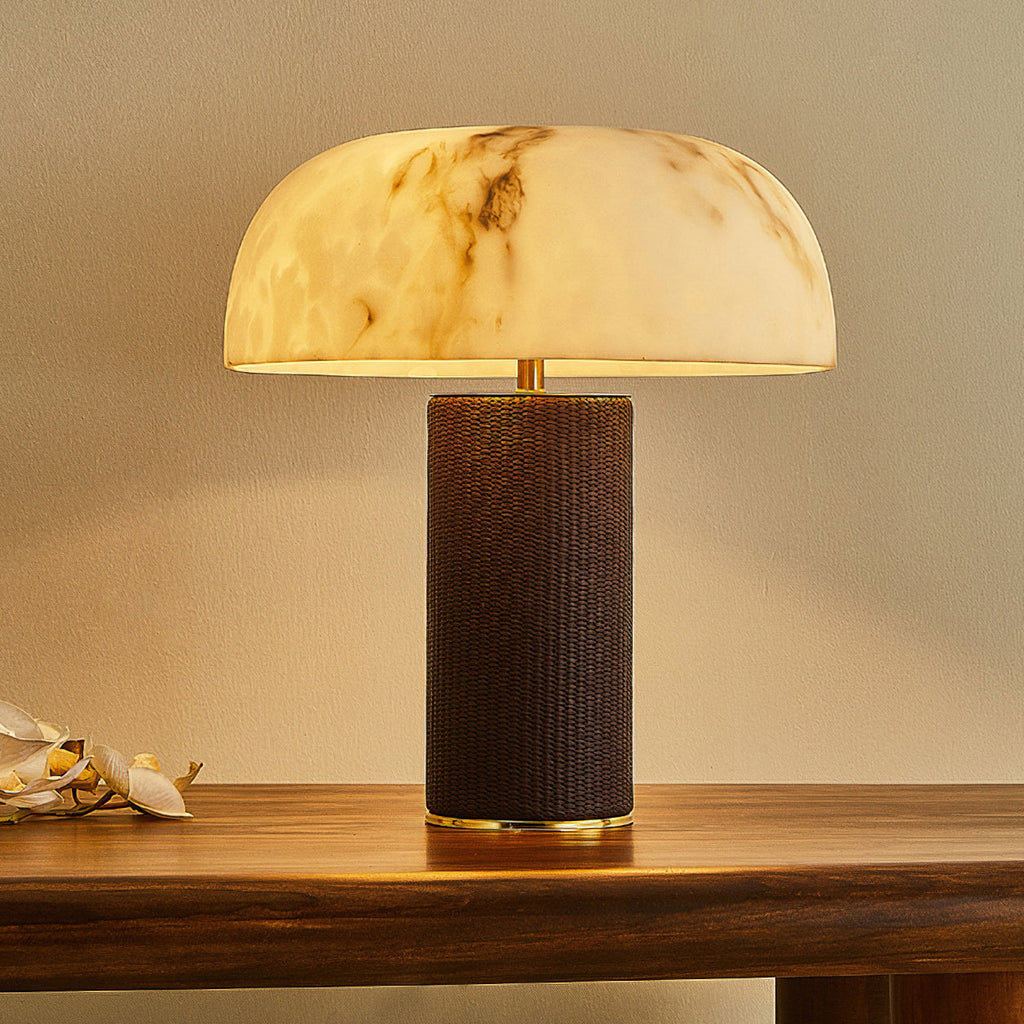 Clérachic table lamp lit warm, with a wide domed shade, brass-toned trim and a dark base, on a wooden table.
