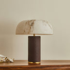 Unlit Clérachic table lamp with a marbled white shade and a dark woven base, on a wooden table against a cream wall.