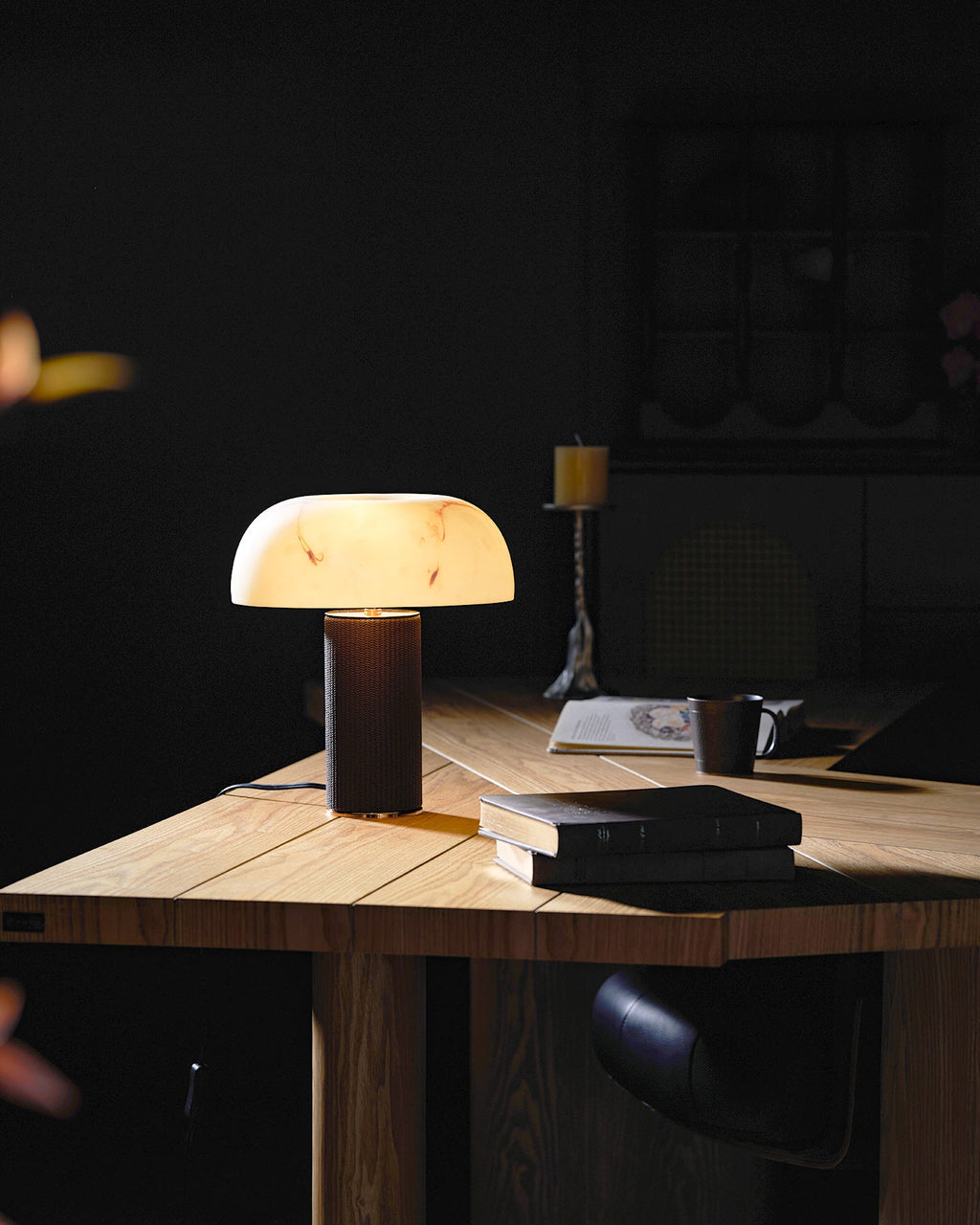 Small lit Clérachic table lamp on a wood desk in a dim study, with books and a mug in front.