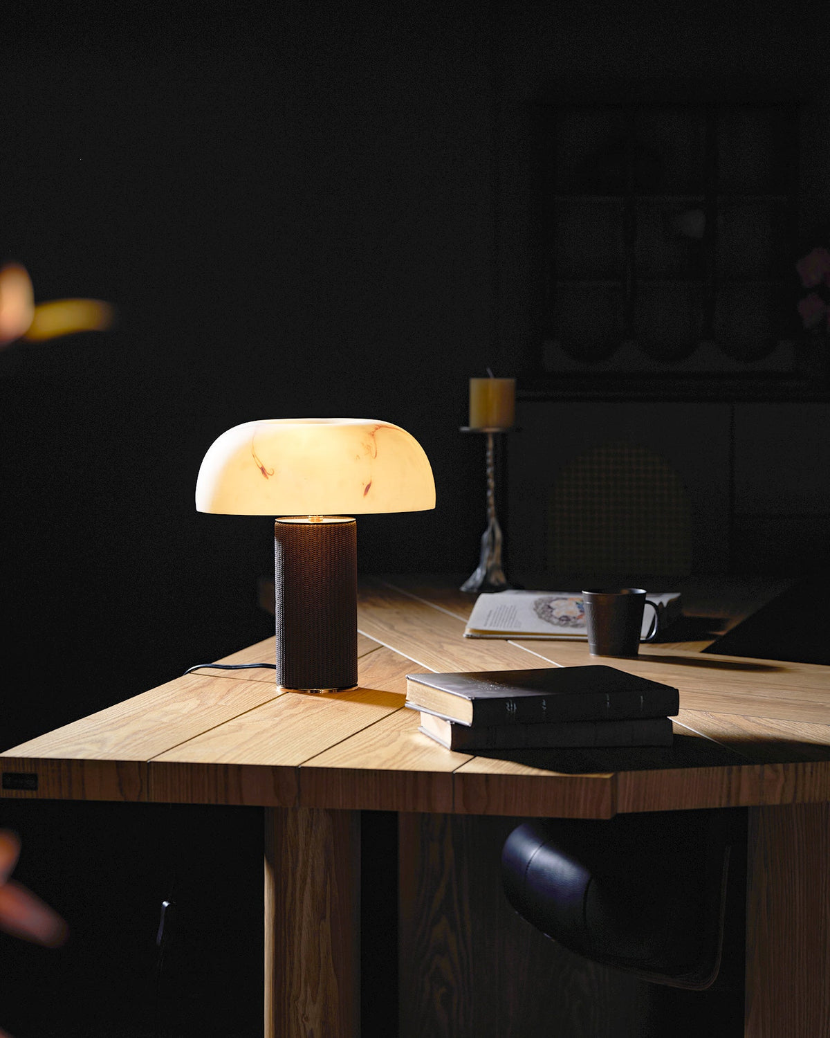 Small lit Clérachic table lamp on a wood desk in a dim study, with books and a mug in front.