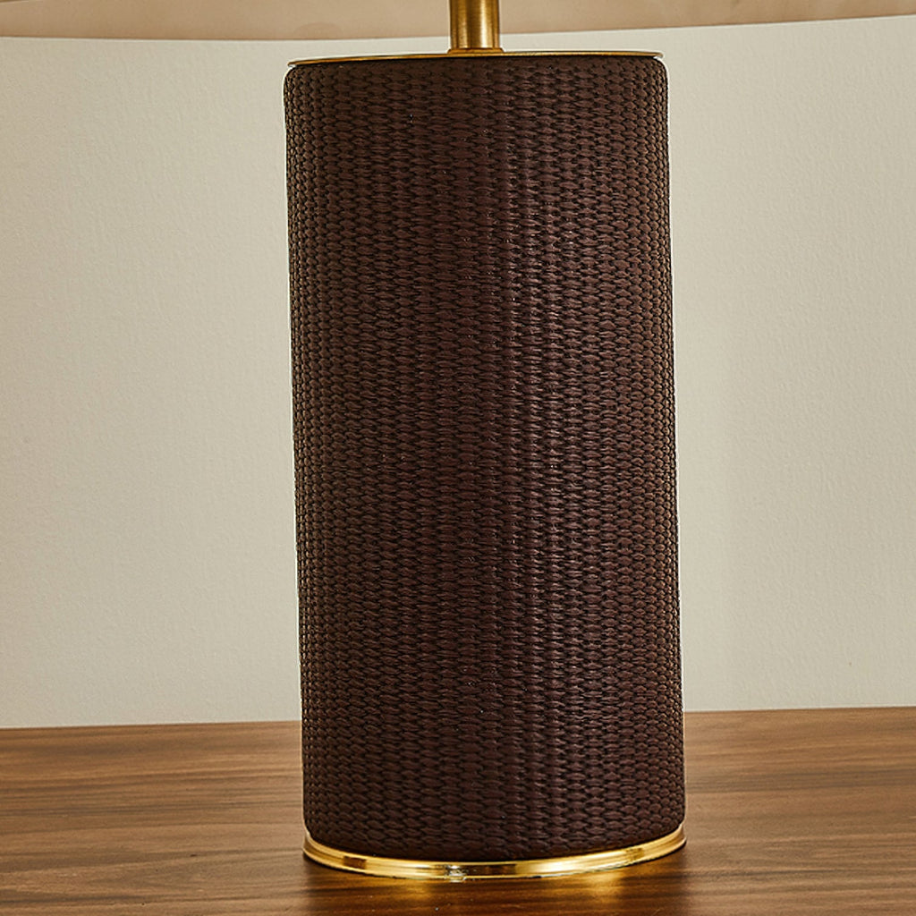 Close view of the dark brown woven-leather base of this Clérachic table lamp, with a gold band at its foot and a brass stem above.