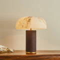 A Clérachic table lamp lit on a wooden table, with white orchids to the left and a cream wall behind.