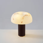 Clérachic table lamp lit on a pale table against a soft blue-grey backdrop, with a rounded marbled shade and a dark base.