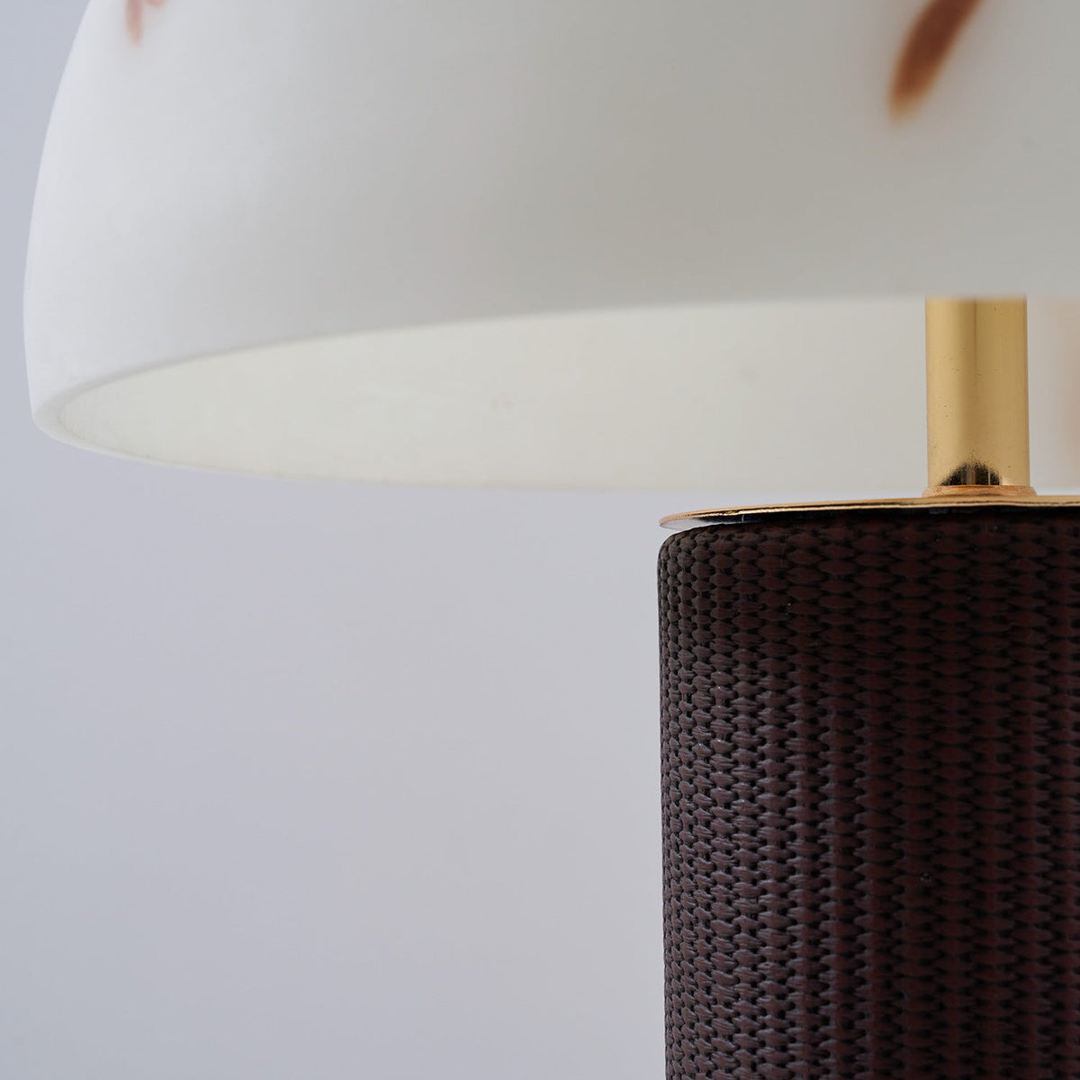 Underside of the shade and the brass stem of this Clérachic table lamp, above the dark woven base with a gold ring.