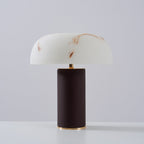 Unlit Clérachic table lamp with a white veined shade and a dark woven base with a gold ring, on a light backdrop.