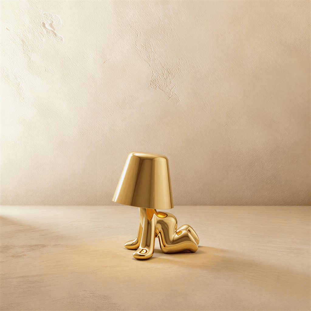 Clérachic gold figurine table lamp reclining on its side, warm glow beneath a tapered shade against a plaster wall.