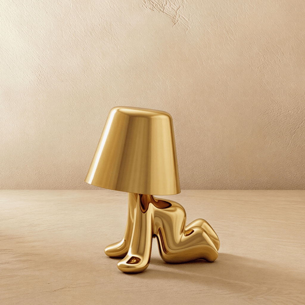 Clérachic gold figurine table lamp reclining on its side, shown unlit with its tapered shade against a plaster wall.