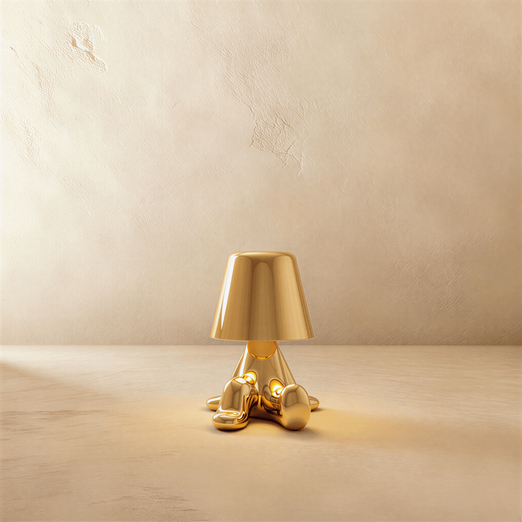 Clérachic gold figurine table lamp seated with hands aglow beneath its tapered shade against a plaster wall.