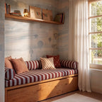 Clérachic gold figurine table lamp glowing warm white on a shelf above a striped daybed in a child's reading nook.
