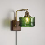 Clérachic fish-scale glass wall sconce in green, its plug-in cord running down the wall from the walnut block.