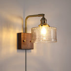 Clérachic fish-scale glass wall sconce in clear glass, the open foot of the drum casting light straight down the wall.