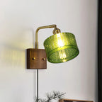 The Clérachic fish-scale glass wall sconce with its shade tilted down on the knuckle joint to aim light onto a book.