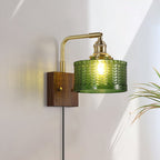 Clérachic fish-scale glass wall sconce mounted low beside a plant, afternoon sun striking the walnut block and green glass.