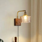 Clérachic fish-scale glass wall sconce in clear glass against pale wood panelling, its plug-in cord dropping to the floor.