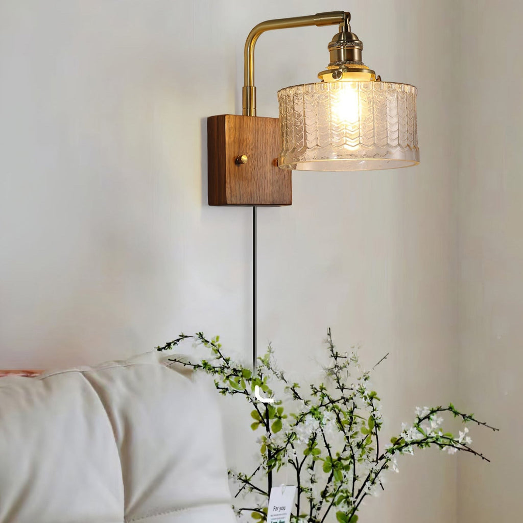 Clérachic fish-scale glass wall sconce above a bed, the clear pressed glass reading amber-gold over white pillows and blossom.