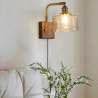 Clérachic fish-scale glass wall sconce above a bed, the clear pressed glass reading amber-gold over white pillows and blossom.