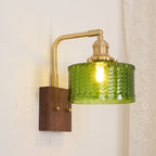 Three-quarter view of the Clérachic fish-scale glass wall sconce, brass arm angled out to carry the lit green glass drum.