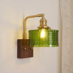Clérachic fish-scale glass wall sconce lit at dusk, warm light escaping the open foot of the green glass drum onto the wall.