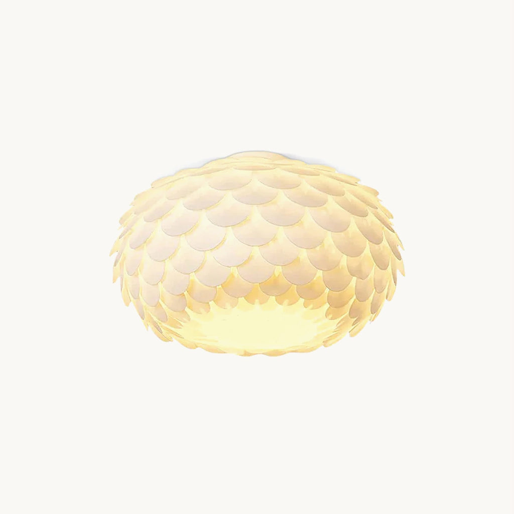White fish-scale ceiling light with overlapping petals and a warm glow from within, this Clérachic oval fitting on a plain backdrop.