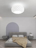 Clérachic oval ceiling light above a low grey upholstered bed with a pale arched panel on the wall behind.