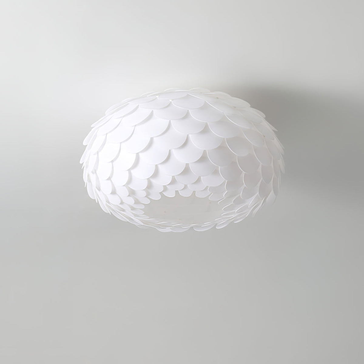 Unlit Clérachic ceiling light with layered white scales, seen from below against a pale grey ceiling.
