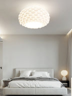 A Clérachic ceiling light in a calm grey bedroom, with a grey upholstered bed and a small round table lamp.