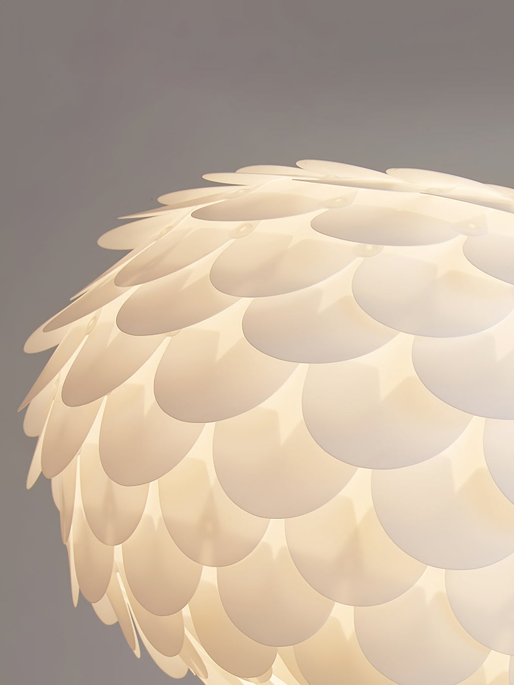 Close view of the overlapping white scales on one side of this lit Clérachic ceiling light, with a warm glow through them.