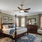 A Clérachic ceiling fan hangs above a four-poster bed with a blue throw, in a bedroom with sage green walls and a dark wood dresser.