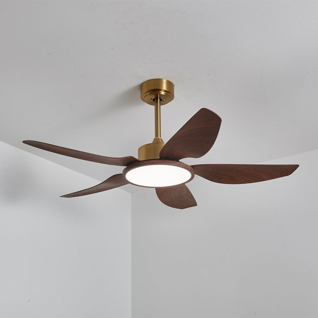 The Clérachic ceiling fan from below with its LED disc lit in a neutral white, against a white ceiling and corner wall.