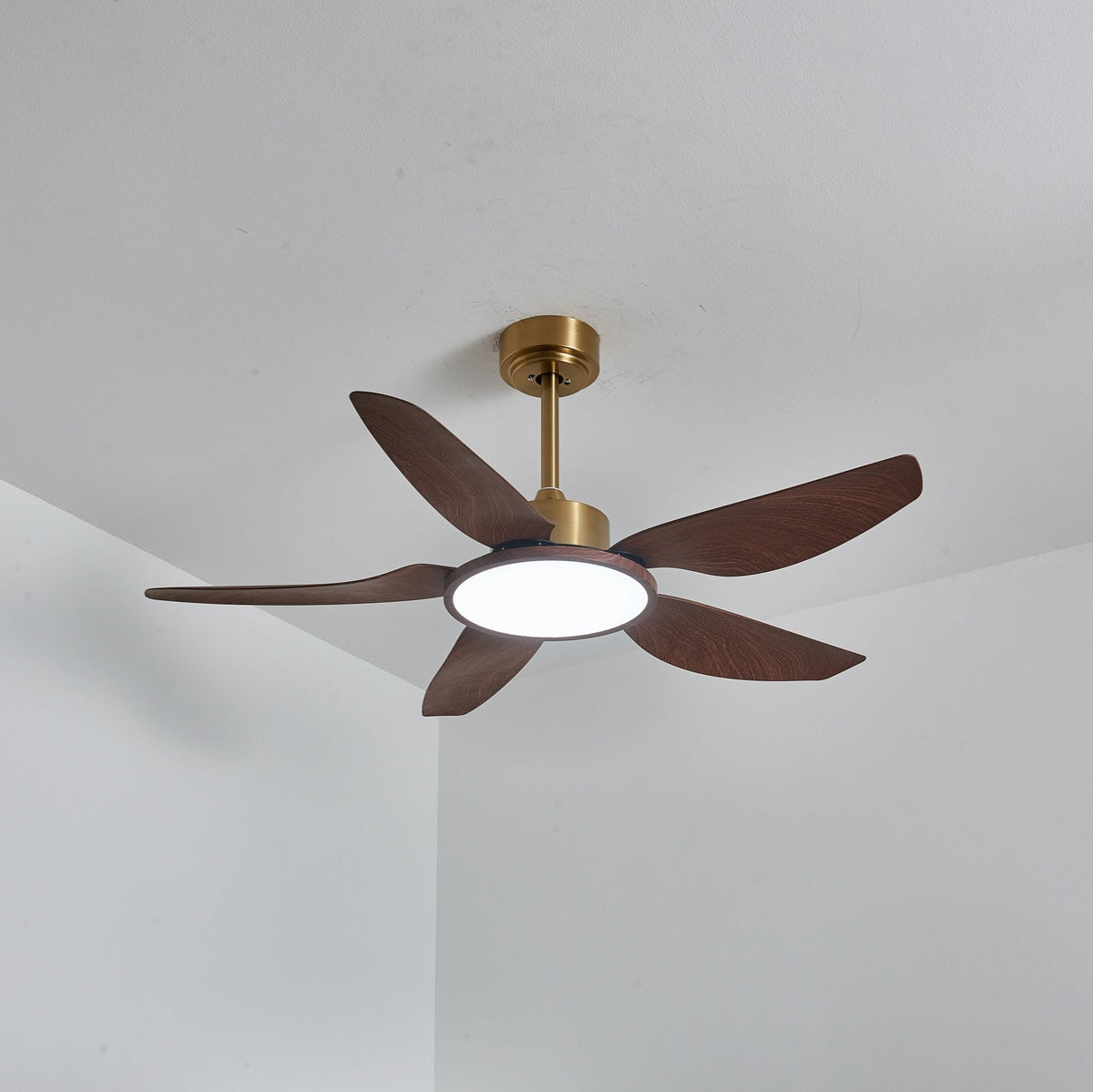 The Clérachic ceiling fan from below with its LED disc lit in a cool white, the blades dark against a pale ceiling.