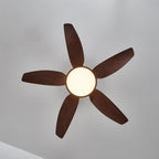 View from directly below of the Clérachic ceiling fan, five walnut-grain blades radiating around a warm-lit round light.