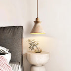 Clérachic travertine pendant with a wooden accent hanging beside a bed, lighting a round stone bedside table