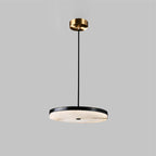 Clérachic Flat Disc Pendant Light on a studio grey backdrop, black metal rim over pale alabaster with a brass ceiling canopy.