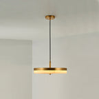 The brass-rim Clérachic Flat Disc Pendant Light lit in a bare white corner, its alabaster edge glowing warm beneath the metal band.