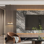 A brass Clérachic Flat Disc Pendant Light lit beside a marble media wall, hanging low over a tan leather armchair in a living room.