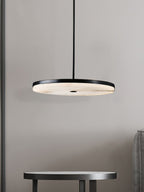 Clérachic Flat Disc Pendant Light hung low over a small round side table, its lit alabaster face throwing a soft pool onto the wall.