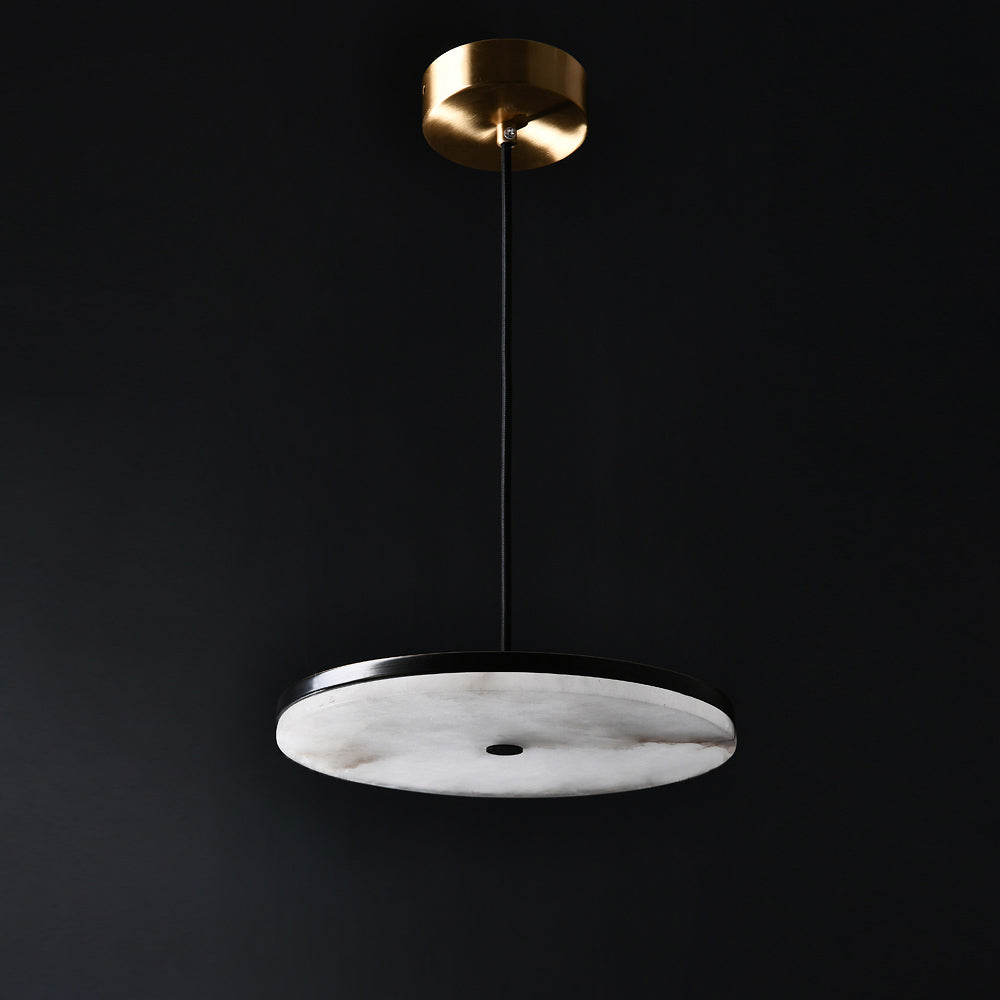 Clérachic Flat Disc Pendant Light unlit on a charcoal backdrop, cool chalk-white alabaster held in a black rim below a brass canopy.