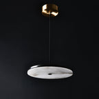 Clérachic Flat Disc Pendant Light unlit on a charcoal backdrop, cool chalk-white alabaster held in a black rim below a brass canopy.