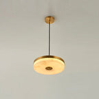 The brass-finish Clérachic Flat Disc Pendant Light on a pale wall, its alabaster shade ringed by a wide brushed brass band.