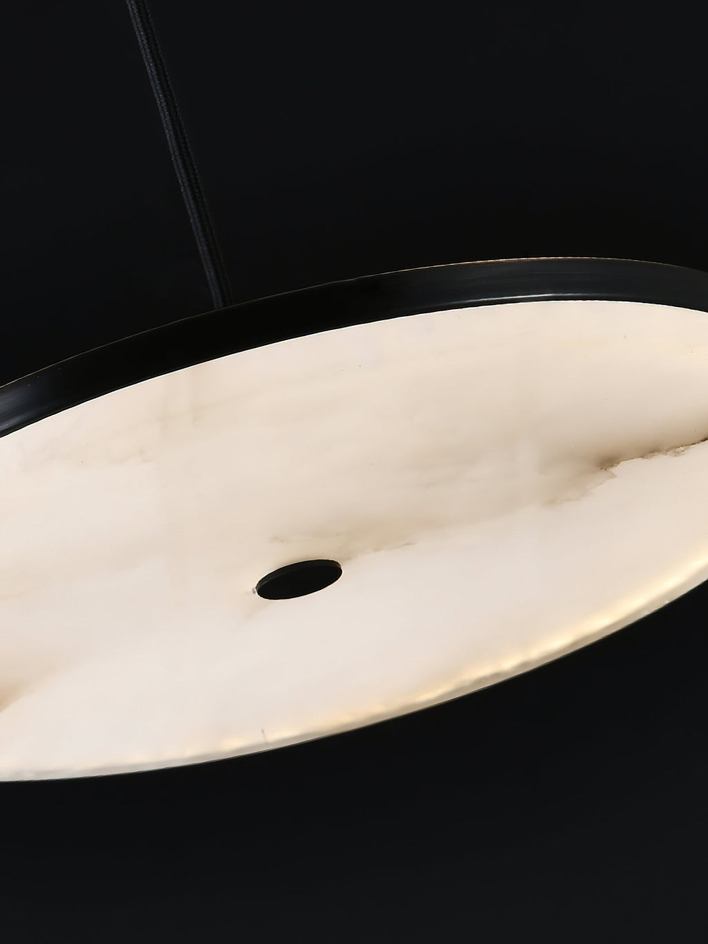 Detail of the Clérachic Flat Disc Pendant Light lit from within, warm honey cream alabaster with brown veining running across it.