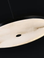 Detail of the Clérachic Flat Disc Pendant Light lit from within, warm honey cream alabaster with brown veining running across it.